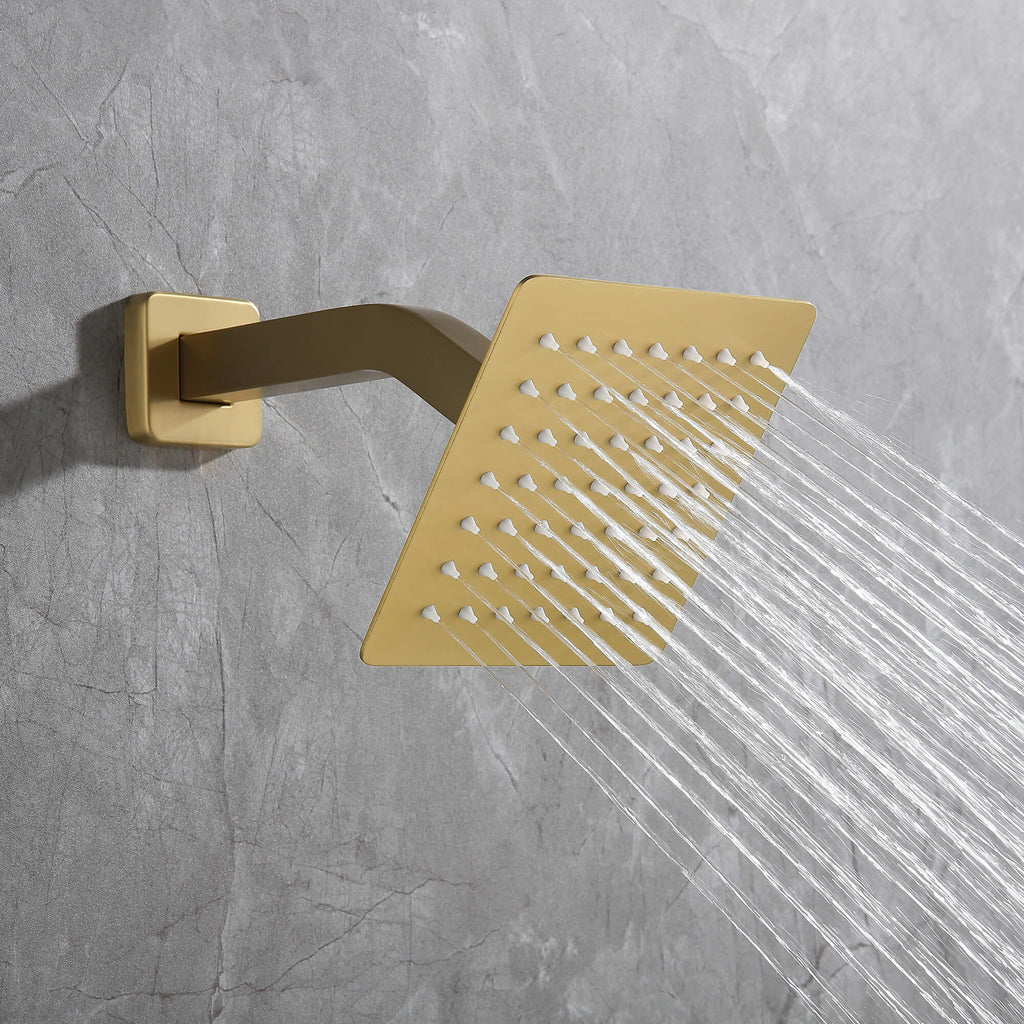 Close-up of brushed gold wall-mounted square shower head with strong spray stream.