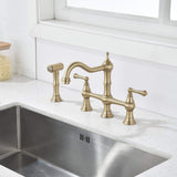 Brushed gold bridge kitchen faucet with side spray installed on a kitchen sink