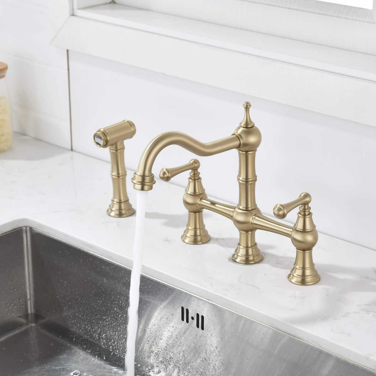 Brushed gold kitchen bridge faucet with high arc spout running over the sink