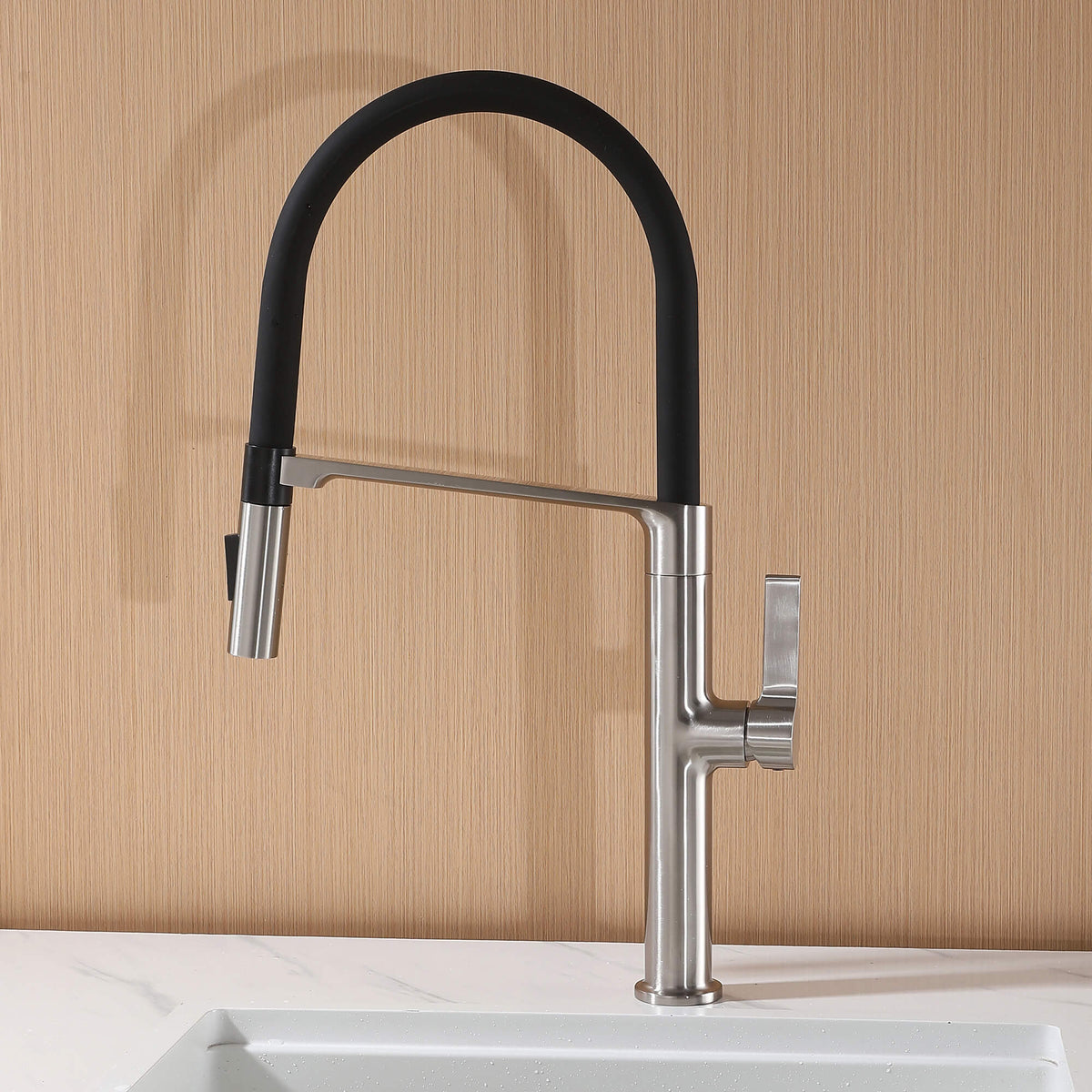 Brushed nickel commercial style kitchen faucet installed on white sink with wood backsplash