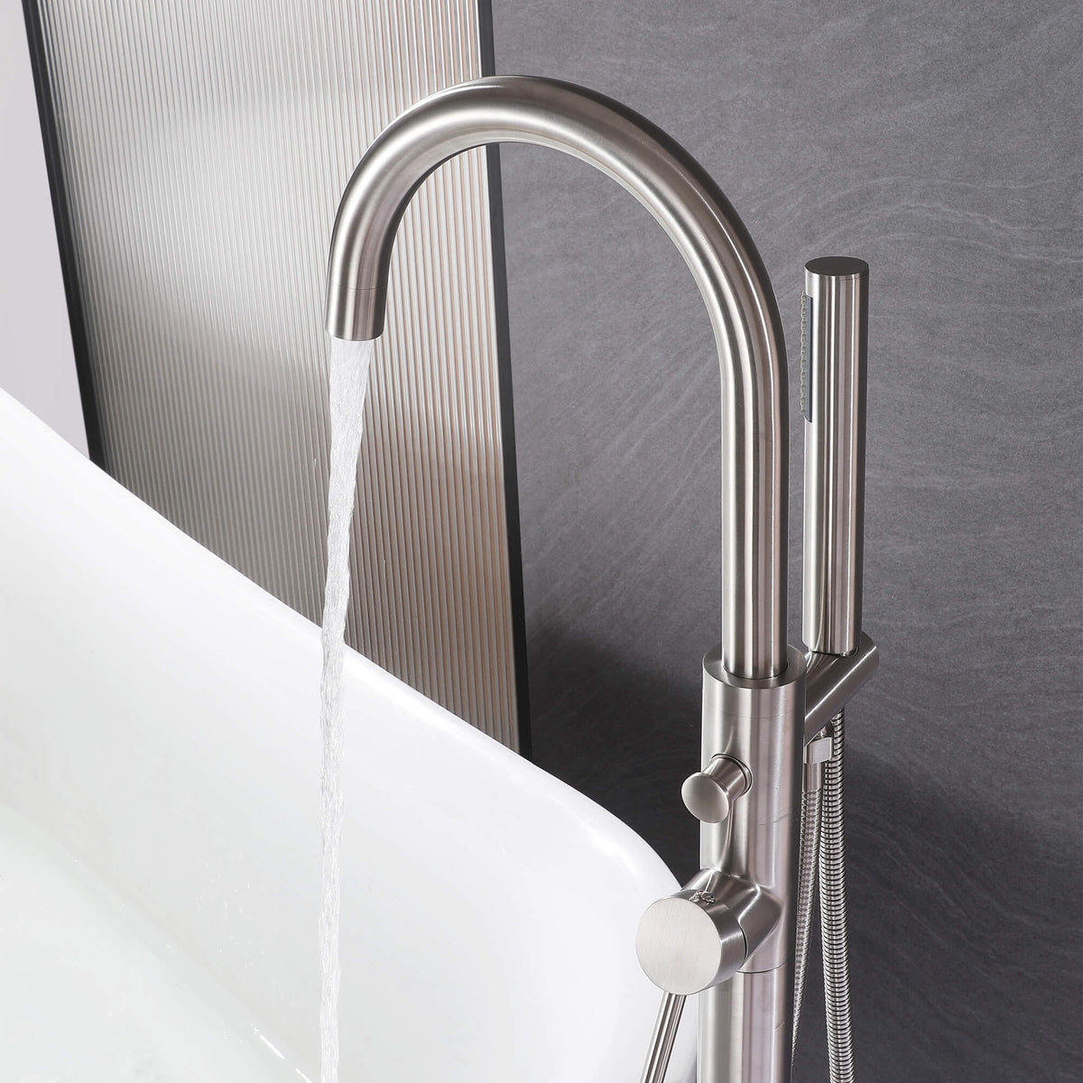 Brushed nickel floor mounted tub faucet running water beside a freestanding bathtub