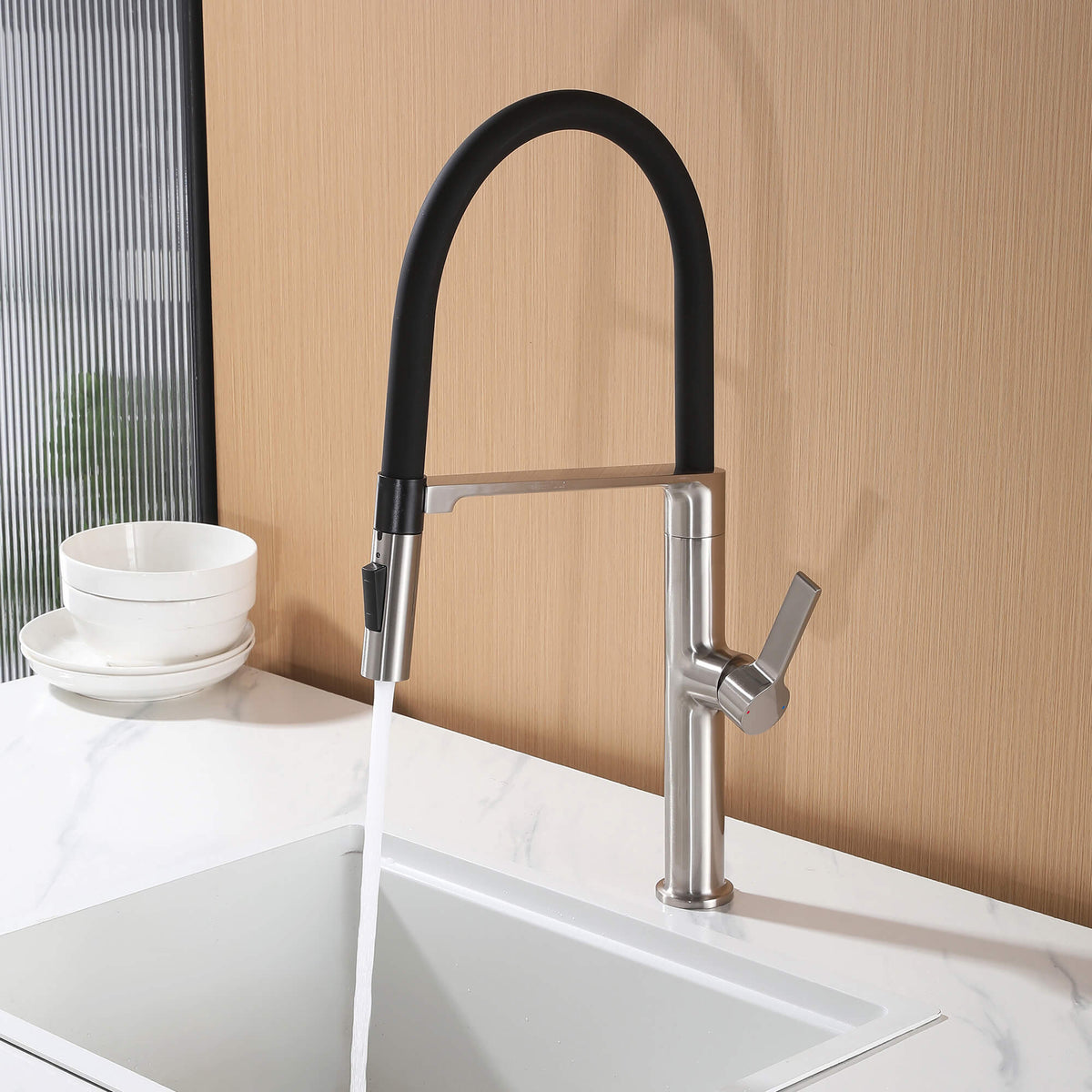 Brushed nickel kitchen faucet with black flexible hose running stream water over kitchen sink
