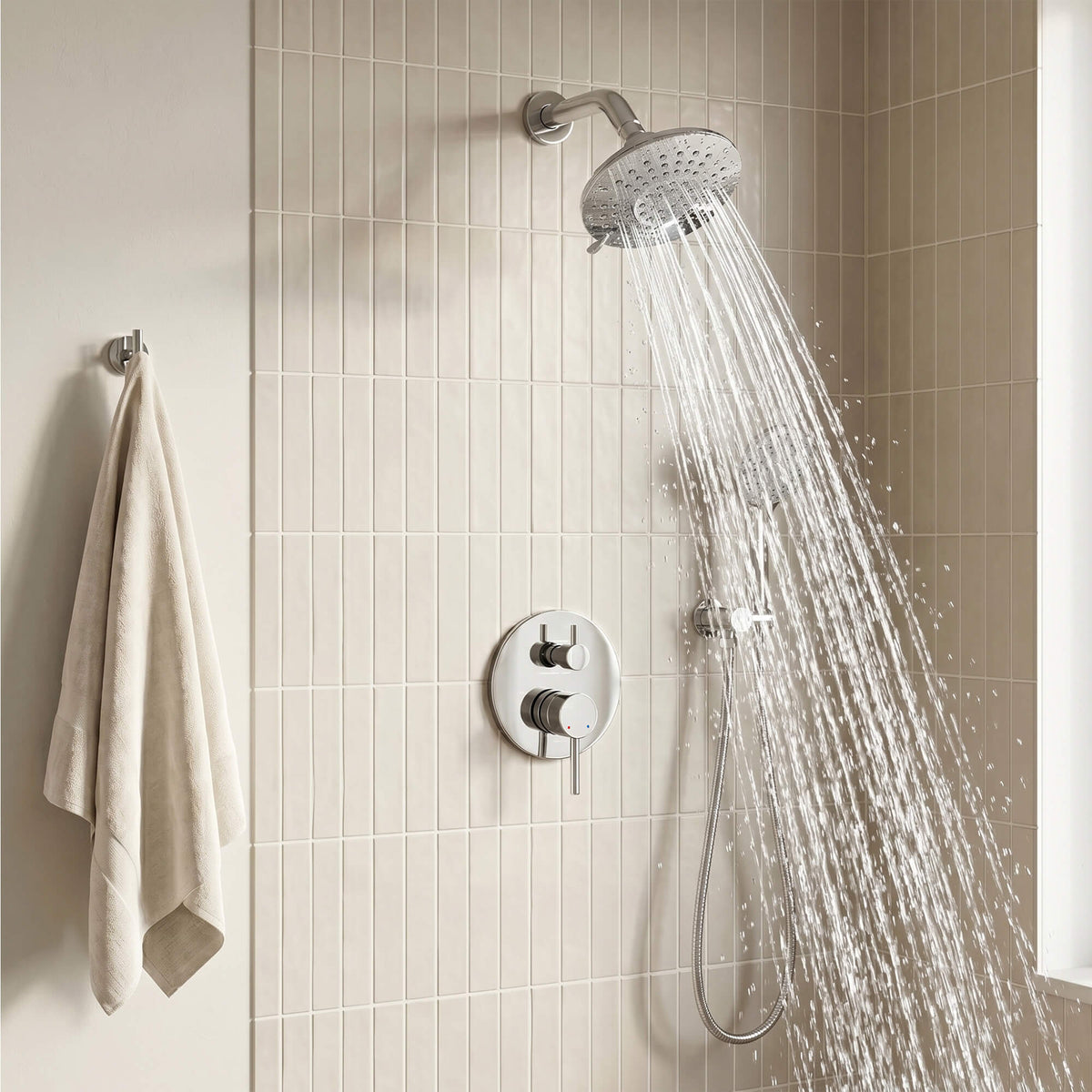 Polished chrome overhead fixture delivering a wide spray beside a coordinated handheld unit in a tiled bathroom