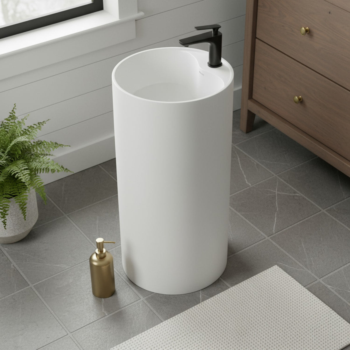 Modern white round pedestal sink installed in a bathroom with classic decor, wall sconces and wood cabinets.
