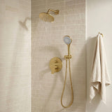 Brushed brass overhead fixture delivering a wide rainfall stream in a warm neutral tiled shower