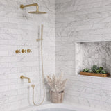 Coordinated gold shower and tub fixtures operating above a white bathtub in a marble-tile bathroom setting