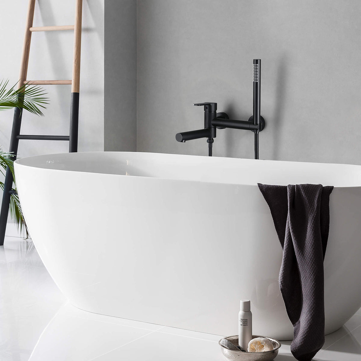 Matte black wall-mount tub filler with hand shower above a freestanding bathtub
