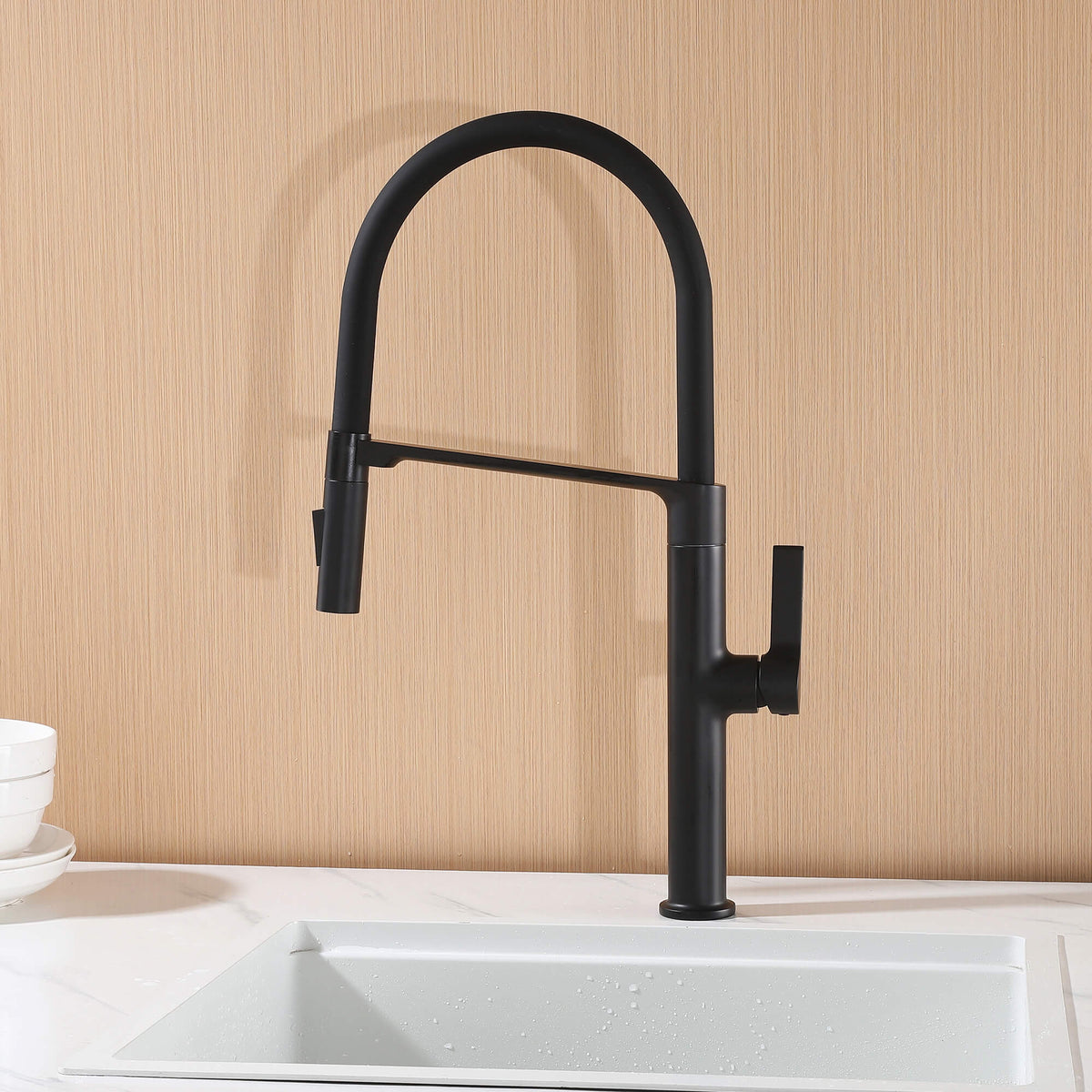 Modern black pull-down faucet mounted beside a white kitchen sink with wood backsplash