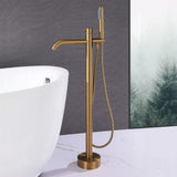 Modern brushed gold floor mount tub filler with handheld shower beside a freestanding bathtub