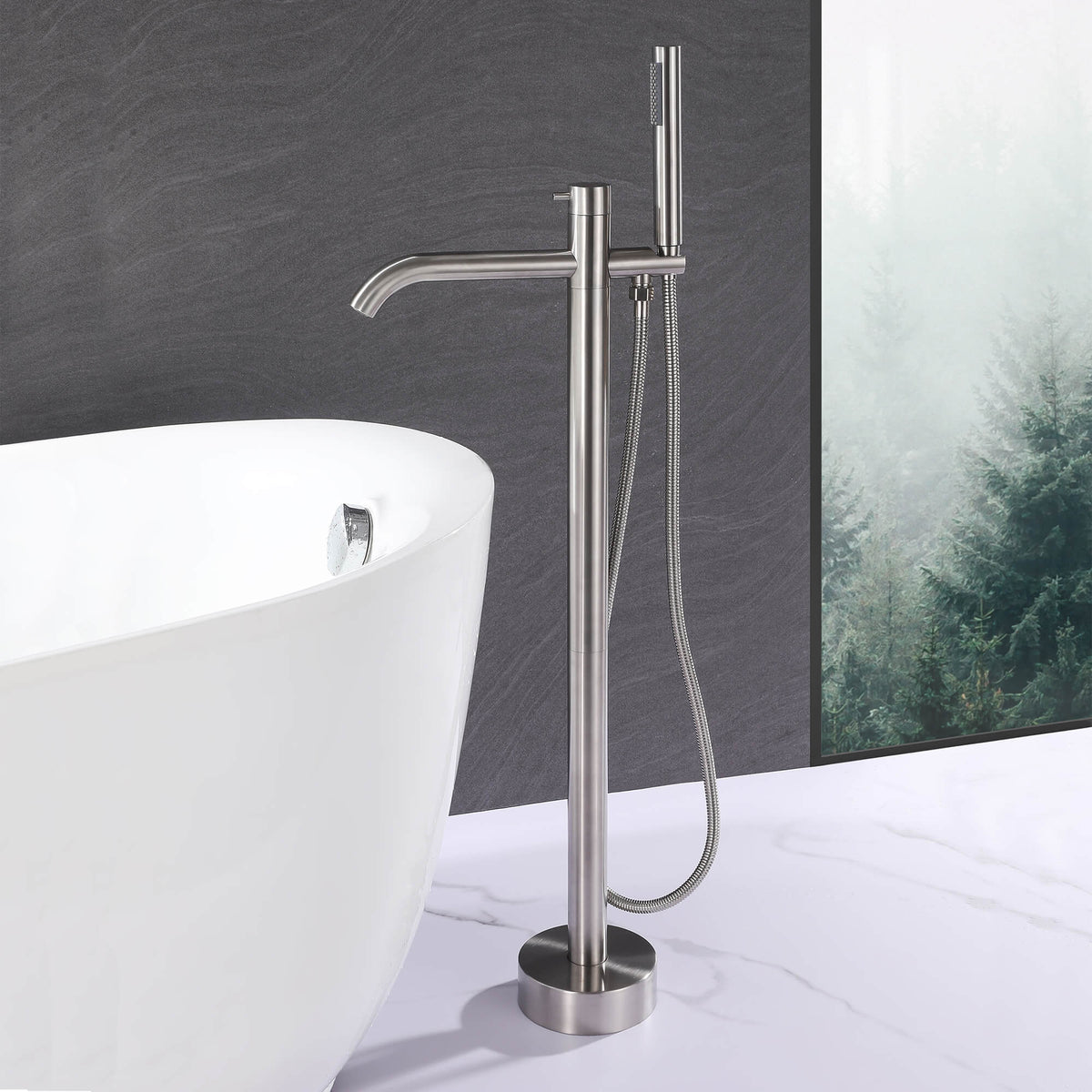 Modern brushed nickel floor mount tub filler with handheld shower beside a freestanding bathtub