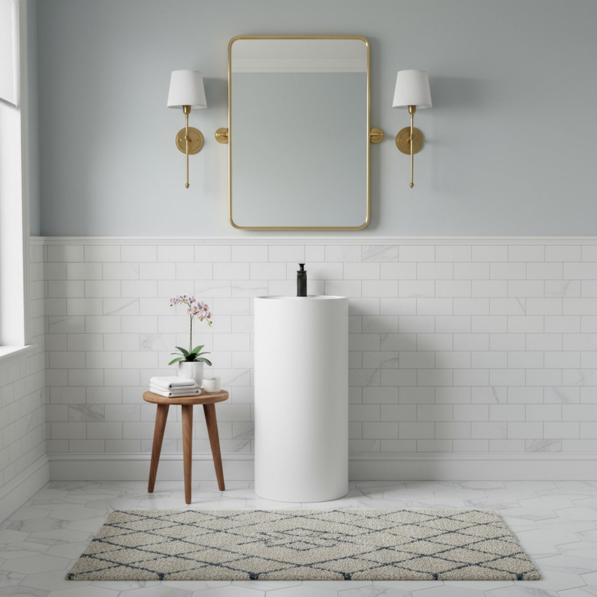 Modern white freestanding pedestal sink with black faucet in bright bathroom with gold mirror and wall sconces.