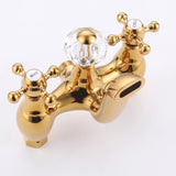 Close-up of polished gold shower mixer with dual cross handles, crystal diverter, and tub spout