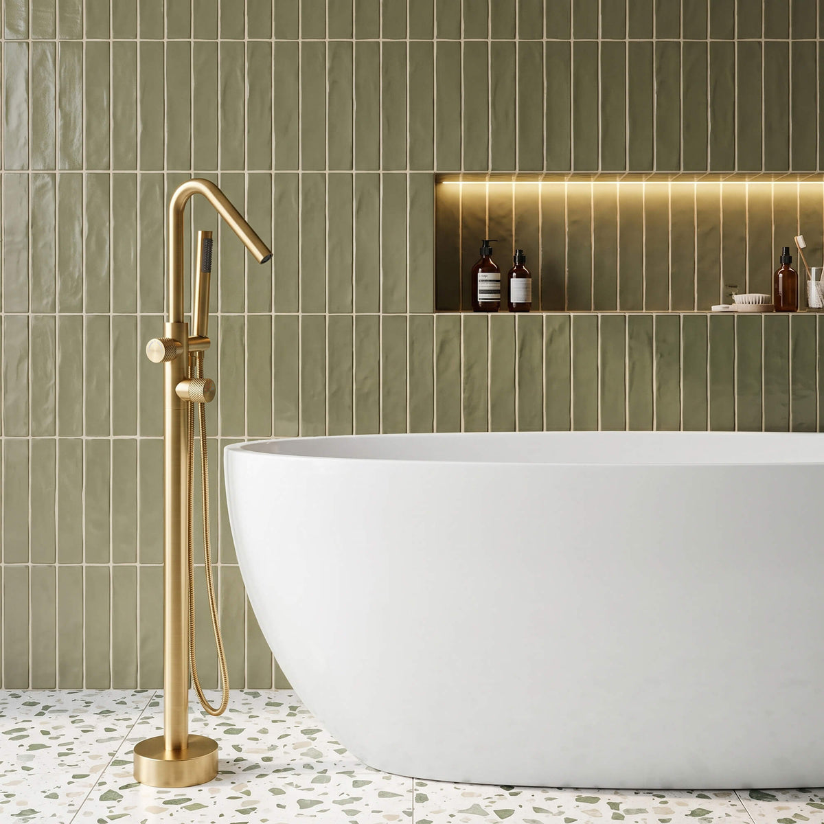 RB1352 brushed gold floor mount tub filler with curved spout and handheld shower beside a white freestanding bathtub.