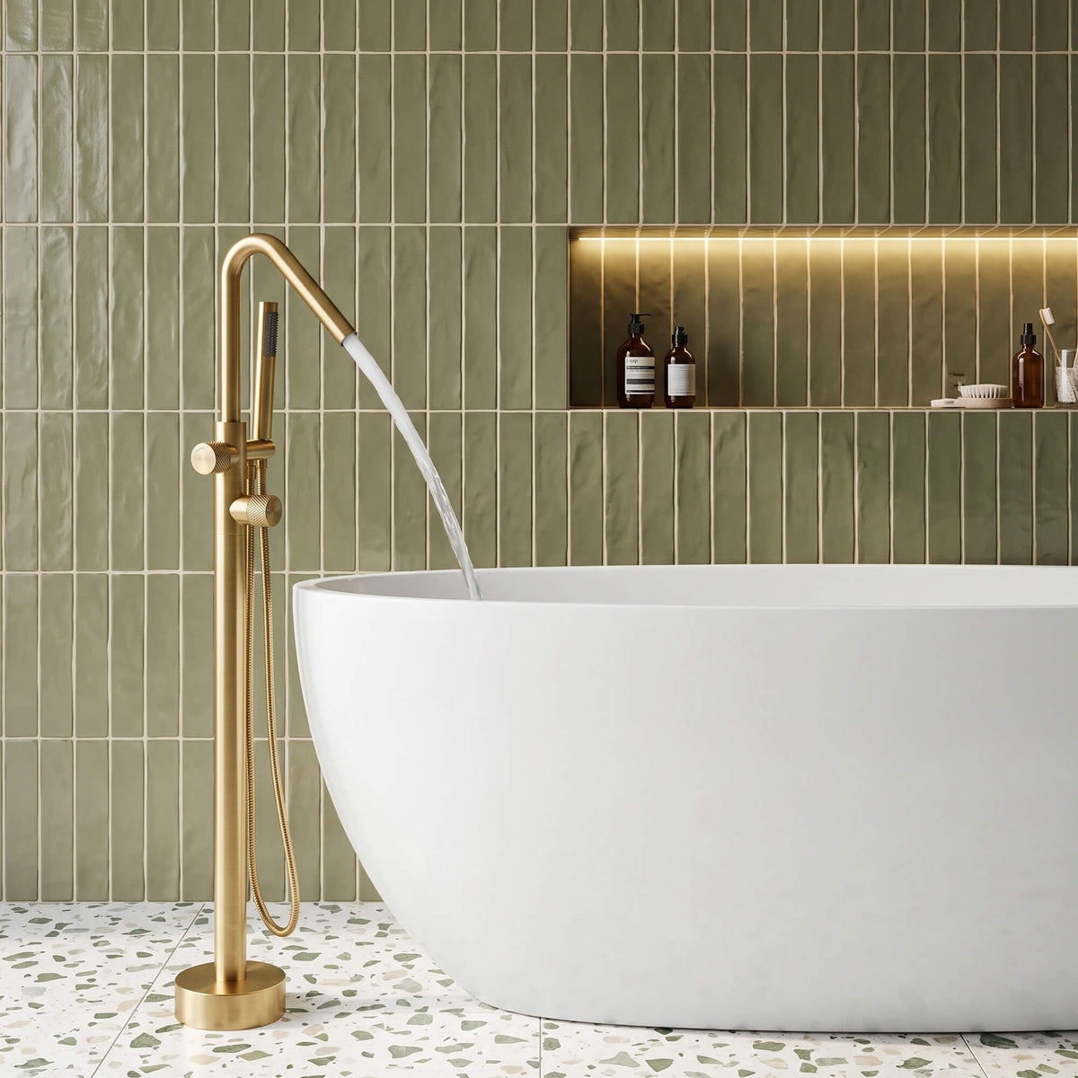 RB1352 brushed gold freestanding bathtub faucet filling a white freestanding bathtub in a modern bathroom with olive green tiles.
